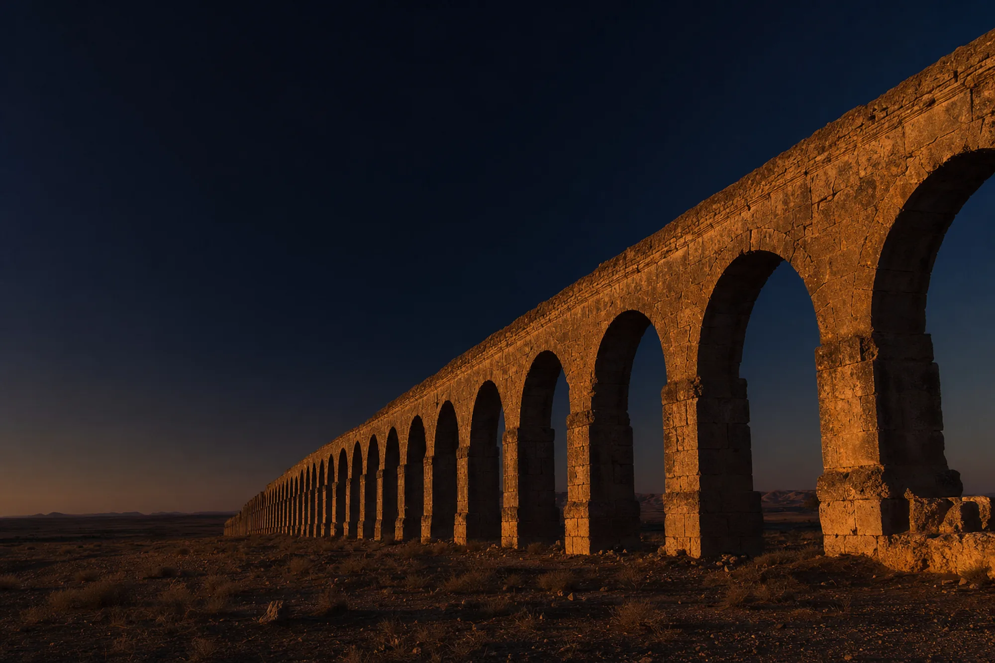 Roman aqueduct arches standing across open ground at dusk