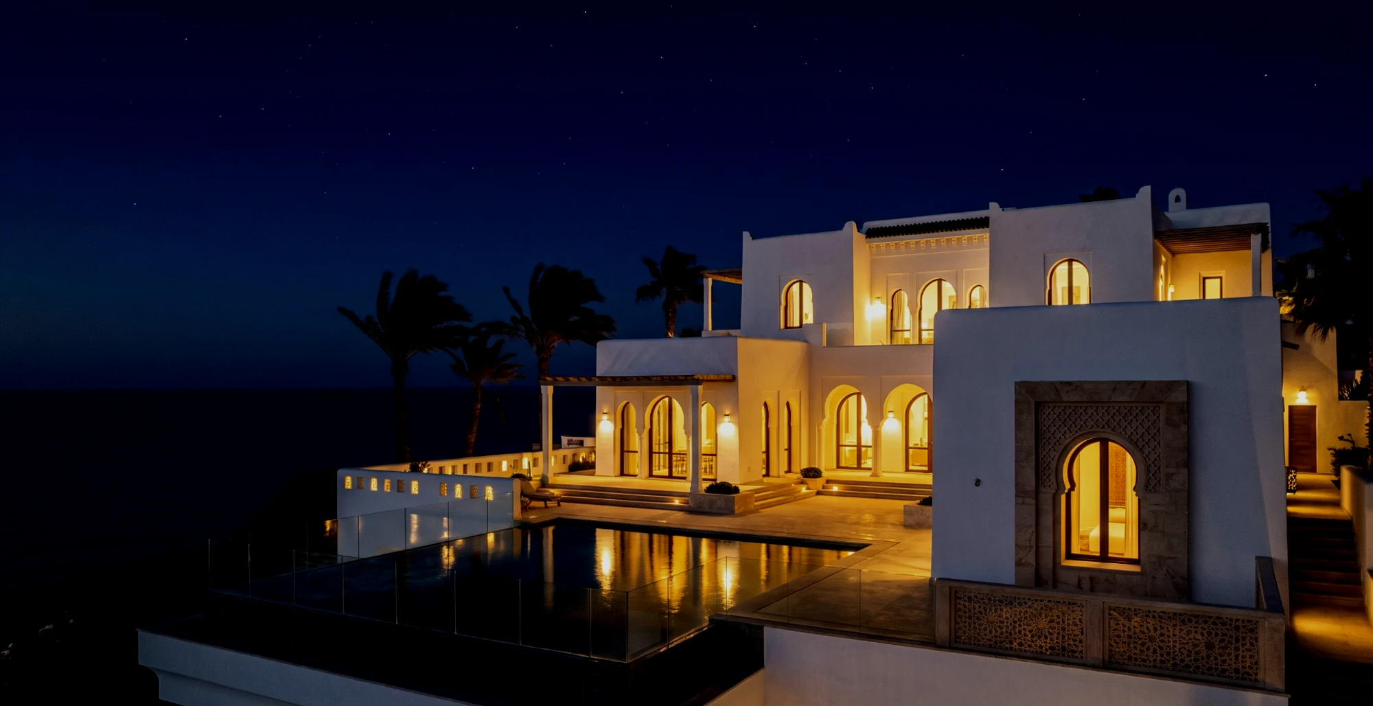 A white villa lit from within, above the sea at night